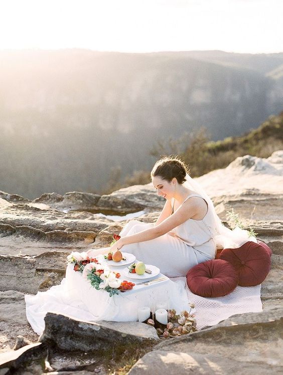 Romantic wedding picnic setting for a mountain elopement with burgundy cushions and table topped with fresh flowers and fruit | We Are Origami